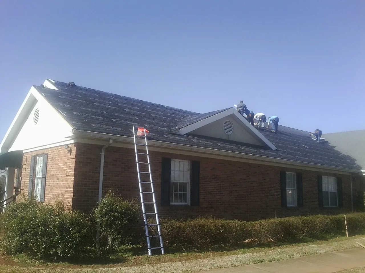 Crew tearing shingles off a brick ranch roof with a ladder set — Metal Roof Repair work by our crew in Swaledale