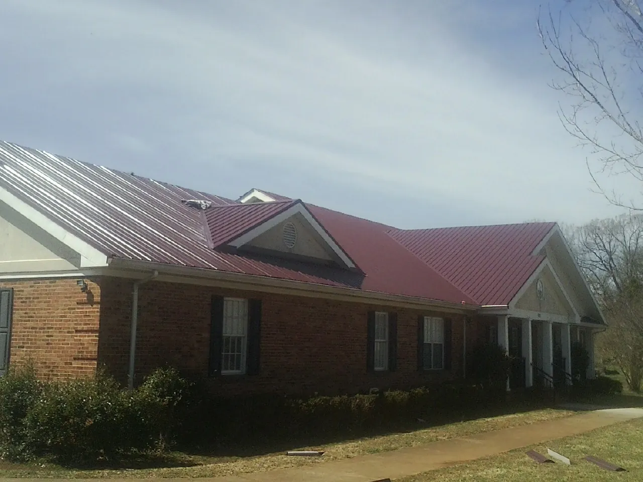 Red metal roof with gabled entries on a long brick building, from a Hail Damage Roof Repair job in Swaledale