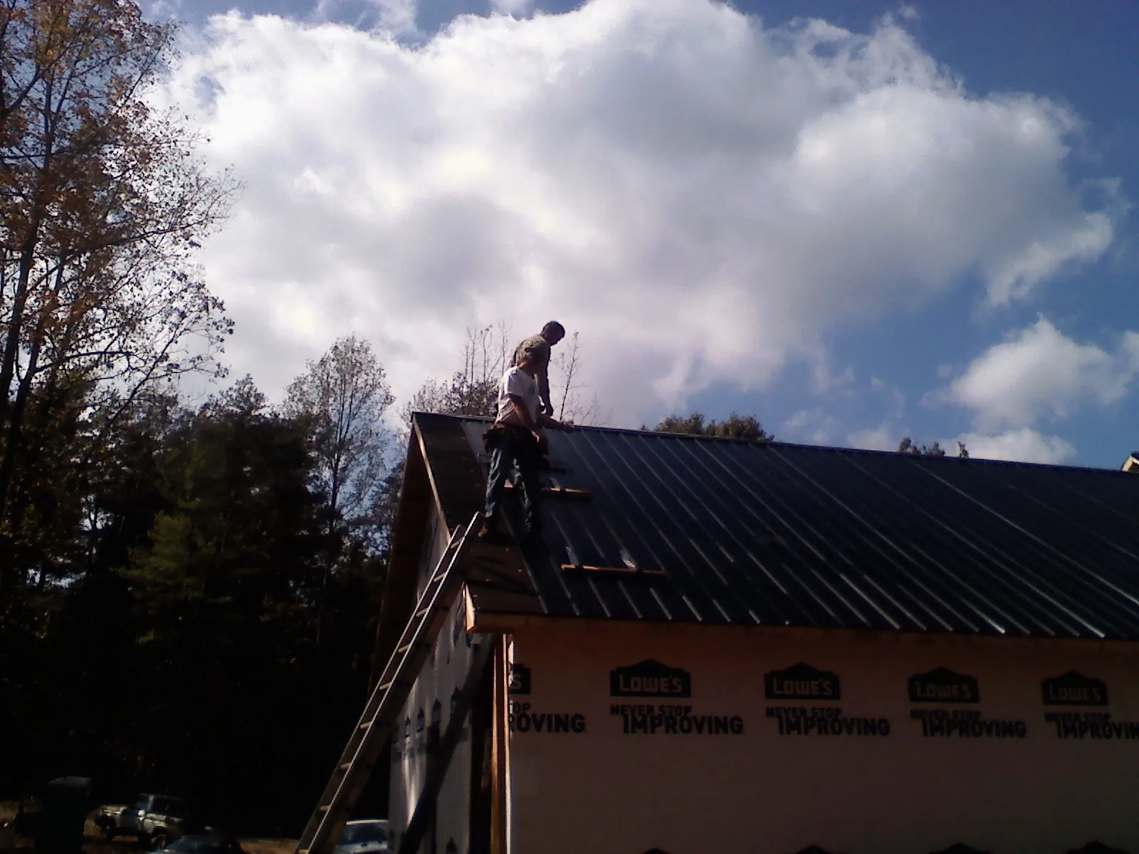 Roofer fastening dark metal panels high against a cloudy sky, from a Roof Inspection job in Swaledale