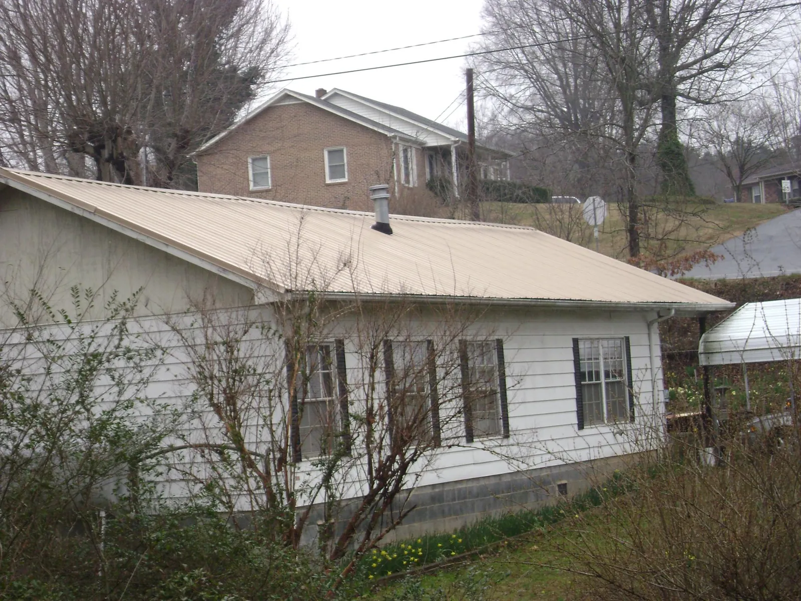 Tan metal roof on a white sided house set into a hillside — Commercial Roofing by Roofing Brothers in Swaledale