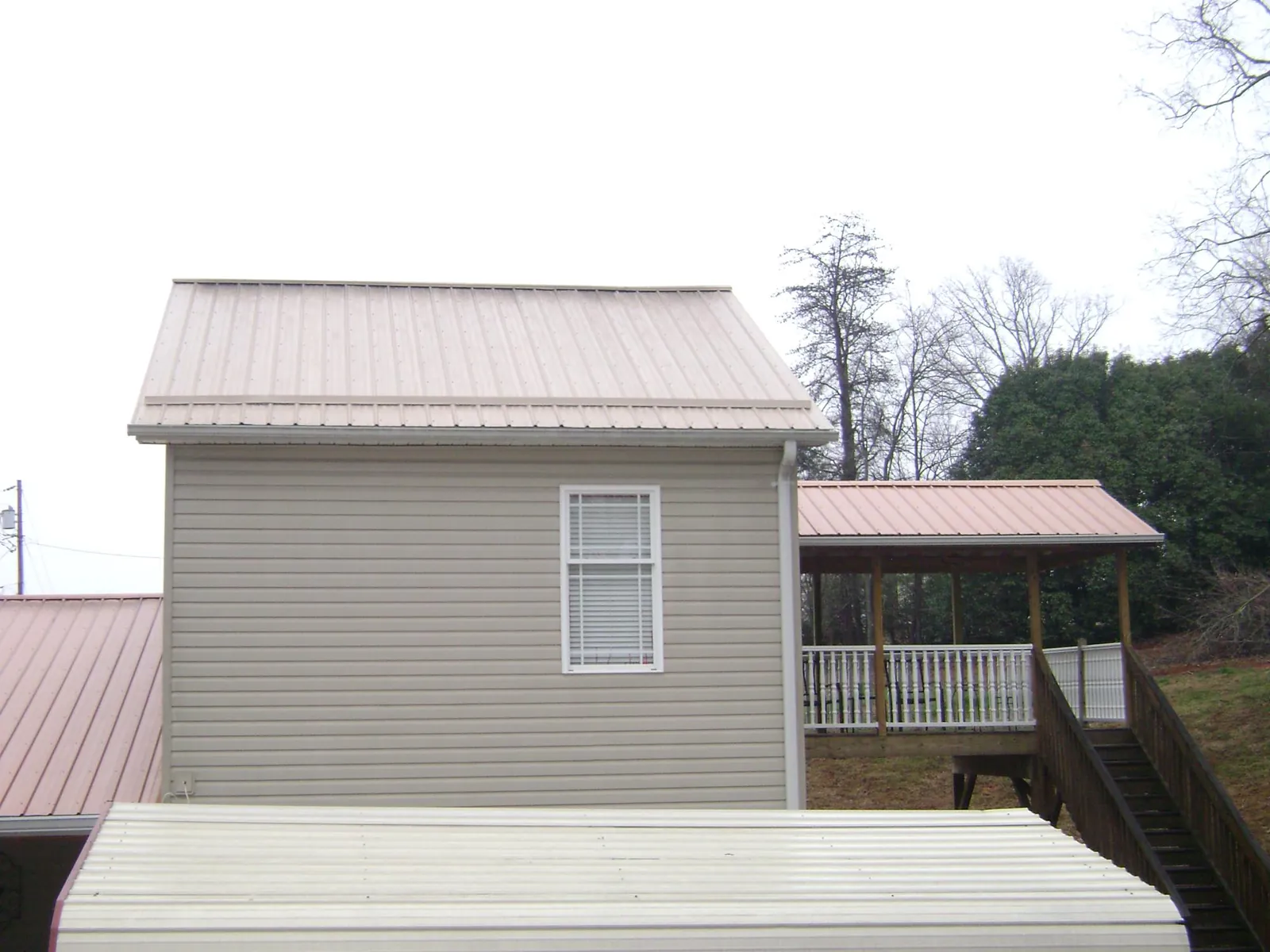 Tan metal roofs on a two story addition and attached porch, from a Roof Replacement job in Swaledale